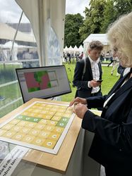 Eine Besucherin legt Spielkarten des Biodiversitätsspiels zu einer Agarlandschaft zusammen.