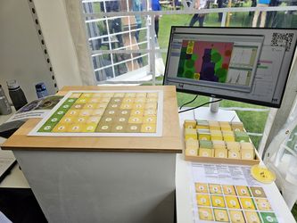 Biodiversitätsspiel "Gestalte Deine Agrarlandschaft" mit Spielkarten und Monitor, auf dem die Modellierung zur Populationsentwicklung der Dunklen Erdhummel gezeigt wird.